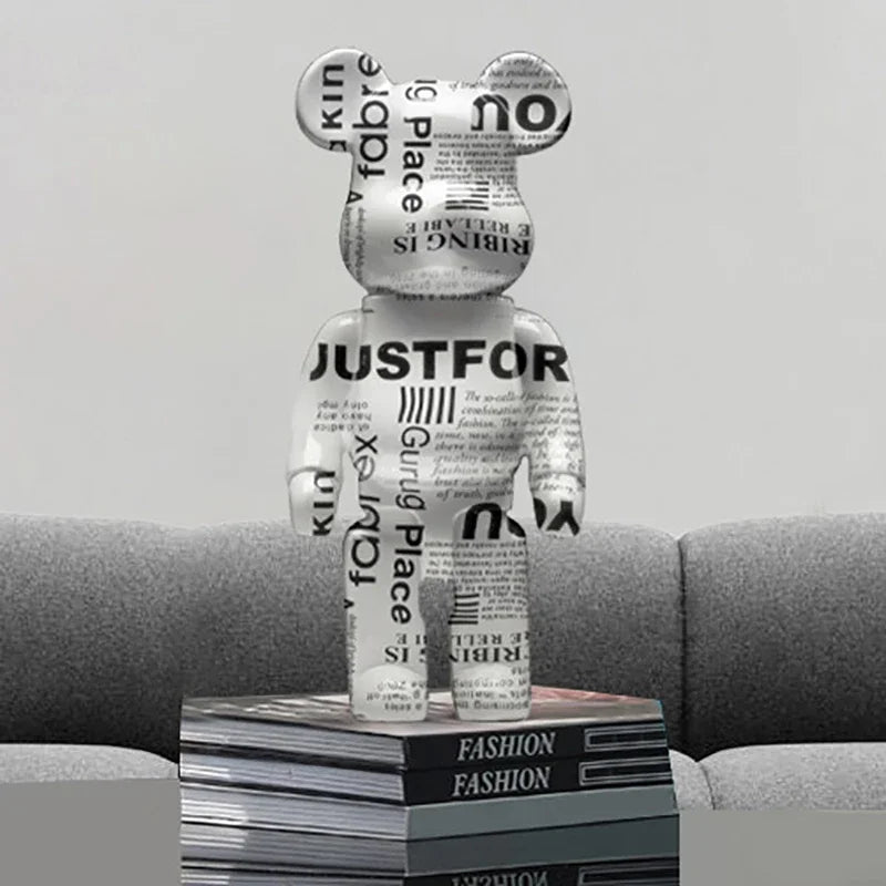Figurine bearbrick design noir et blanc imprimée façon journal, décoration contemporaine posée sur des livres de mode sur un canapé gris