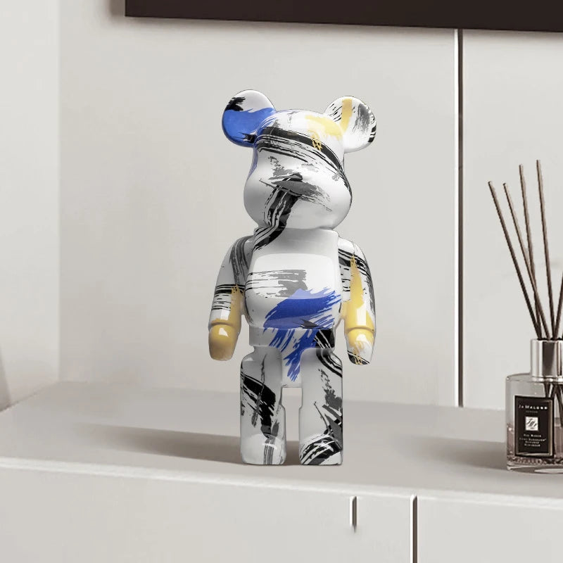 Figurine bearbrick blanche avec motifs abstraits noir, bleu et jaune, déco design posée sur une commode blanche dans un intérieur moderne