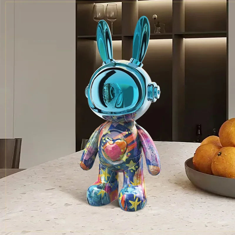 Figurine lapin astronaute au casque bleu chromé et corps multicolore à motifs de cœurs et d’étoiles, posée sur une table design en intérieur moderne