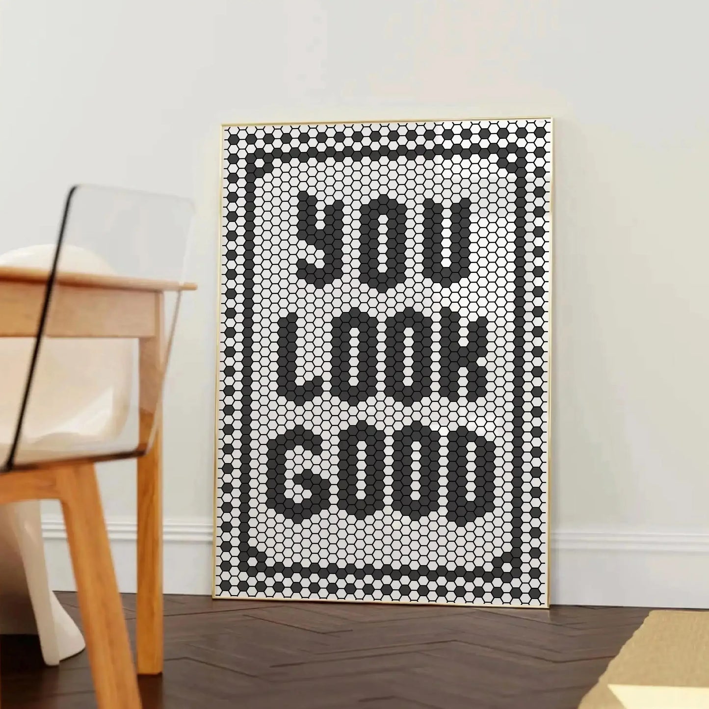 Affiche décorative typographique avec le message “YOU LOOK GOOD” formé par un motif de tuiles hexagonales noires et blanches, encadrée dans un cadre en bois clair, posée contre un mur blanc près d’une chaise design en bois et plexiglas.