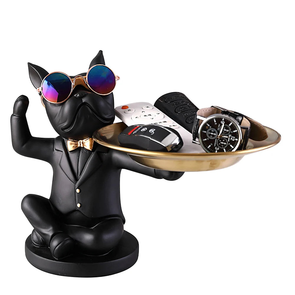 Chien majordome noir en tenue chic, lunettes miroir et plateau doré rempli d’accessoires — une sculpture tendance et pratique pour organiser vos essentiels avec style.