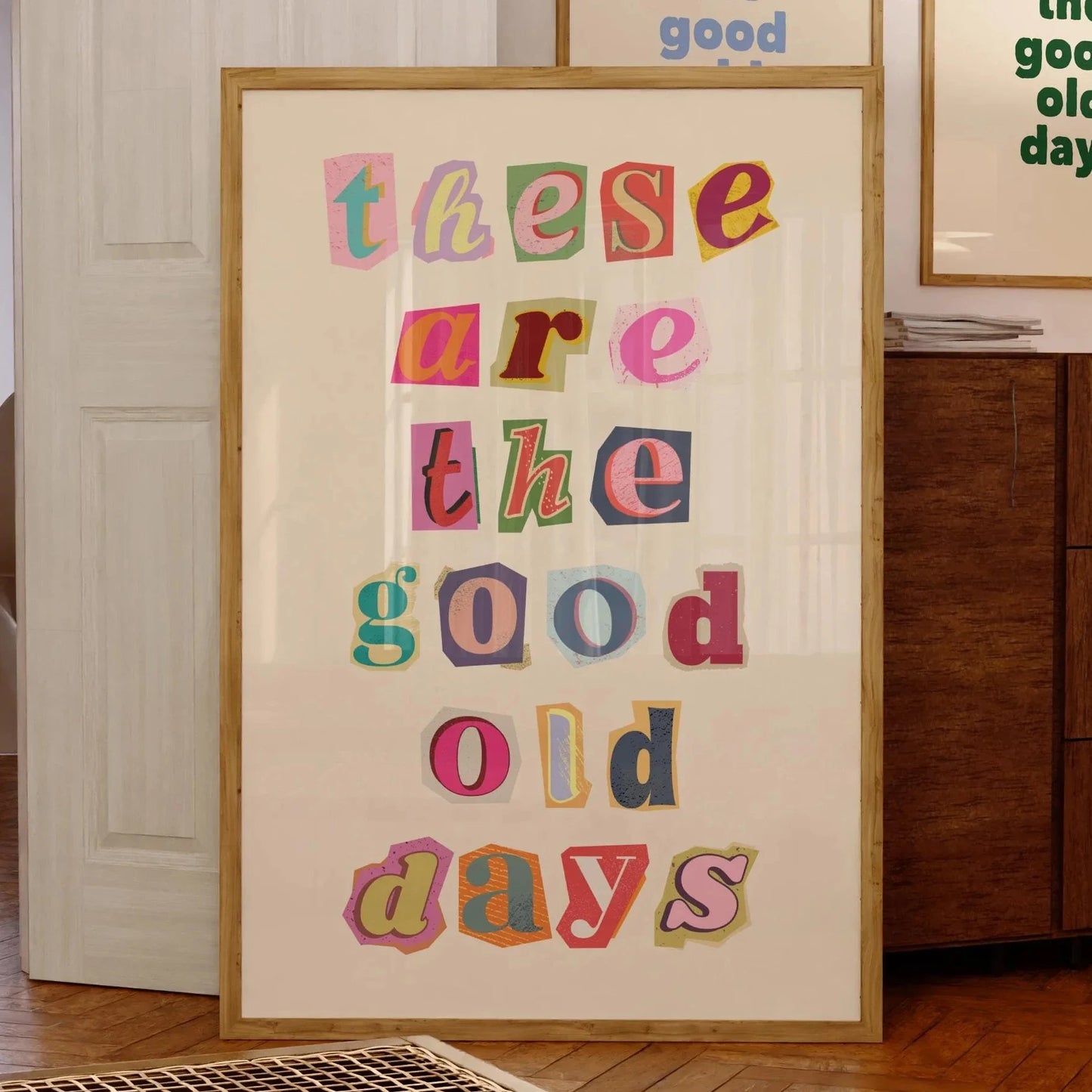 Affiche décorative colorée avec le message “These are the good old days” en lettres découpées de styles variés façon collage, encadrée et posée contre un mur dans un intérieur vintage chaleureux.