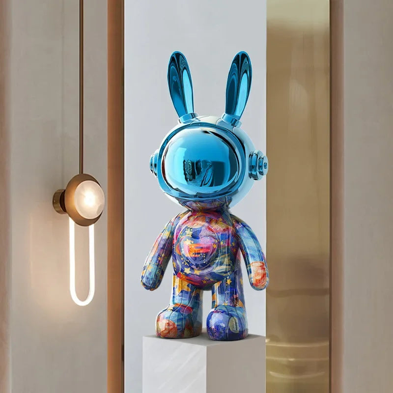 Sculpture lapin futuriste à tête chromée bleu miroir, corps multicolore graffiti, posée sur un socle dans un intérieur design éclairé
