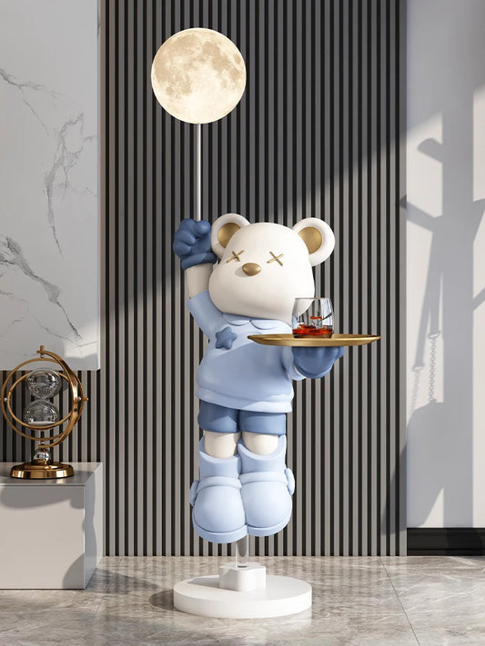 Sculpture ours bleu flottant tenant une lampe lune et un plateau doré avec tasses, décoration pop art originale et fonctionnelle pour intérieur moderne