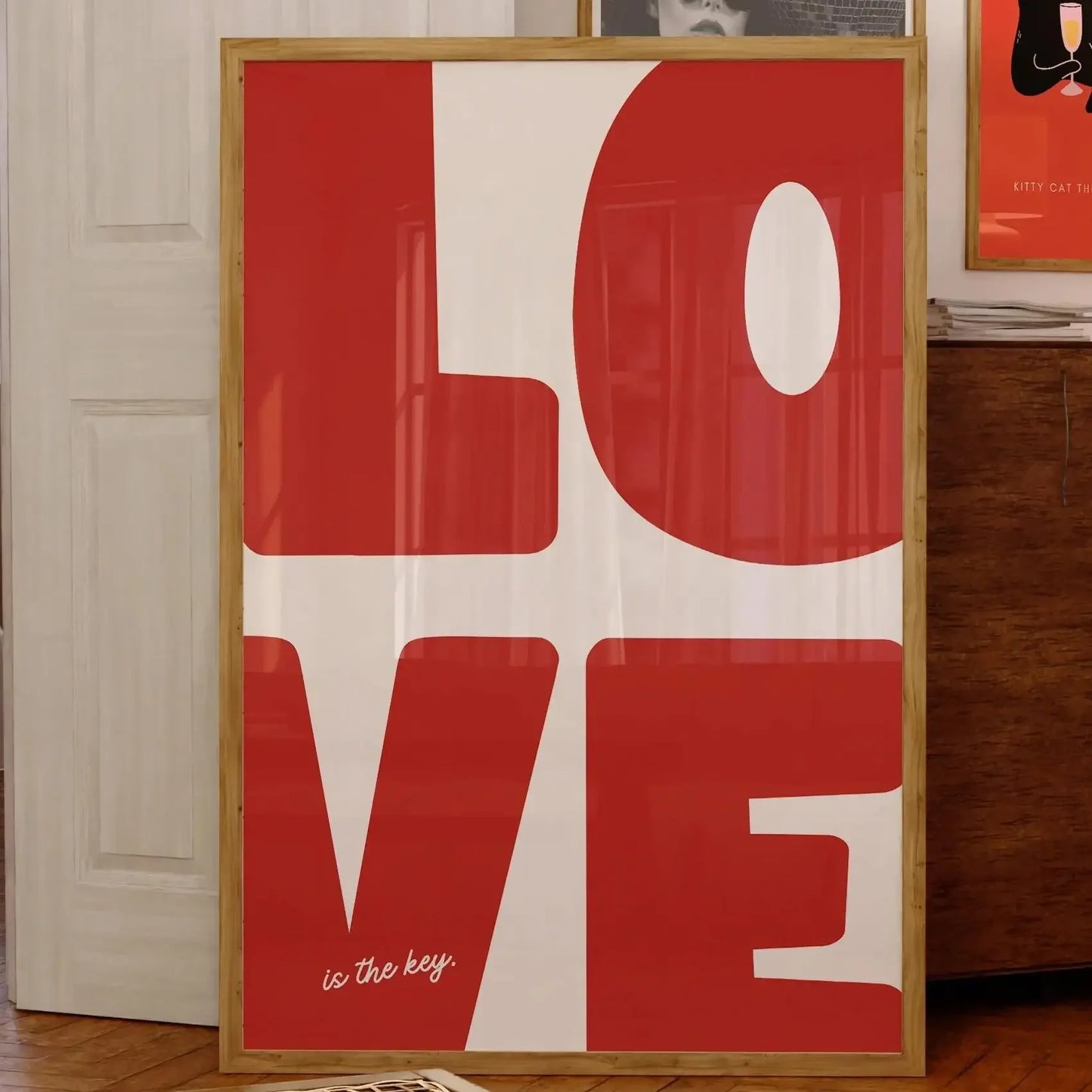 Affiche murale typographique design avec le mot “LOVE” en lettres rouges majuscules sur fond blanc, encadrée en bois et posée dans un intérieur vintage et chaleureux.