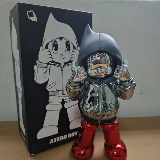 Figurine Astro Boy chromée en hoodie noir et bottes rouges, style chromé street art futuriste, présentée avec sa boîte illustrée en arrière-plan