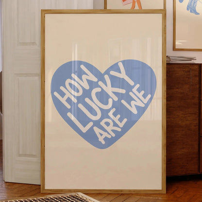 Affiche murale minimaliste avec le message “How Lucky Are We” en lettres blanches sur fond de cœur bleu, encadrée dans un intérieur au style vintage et chaleureux.